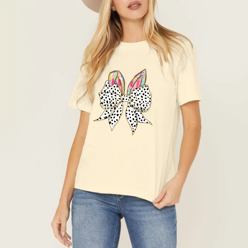 The Bow Is Made Of Black And White Polka Dots, The Bunny Ears Have Colorful Feather-Like Patterns, And The T-Shirt Is Casual.